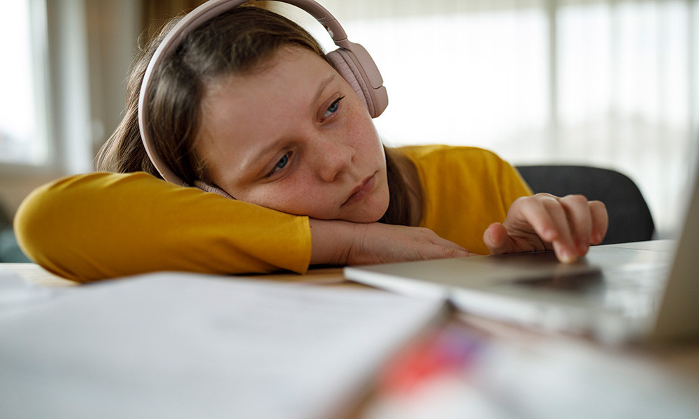 A photo of a bored young girl working on a laptop