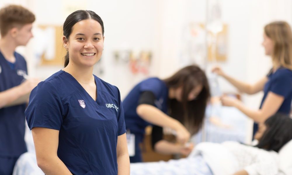 Nursing student standing in simulation lab with other students behind her.