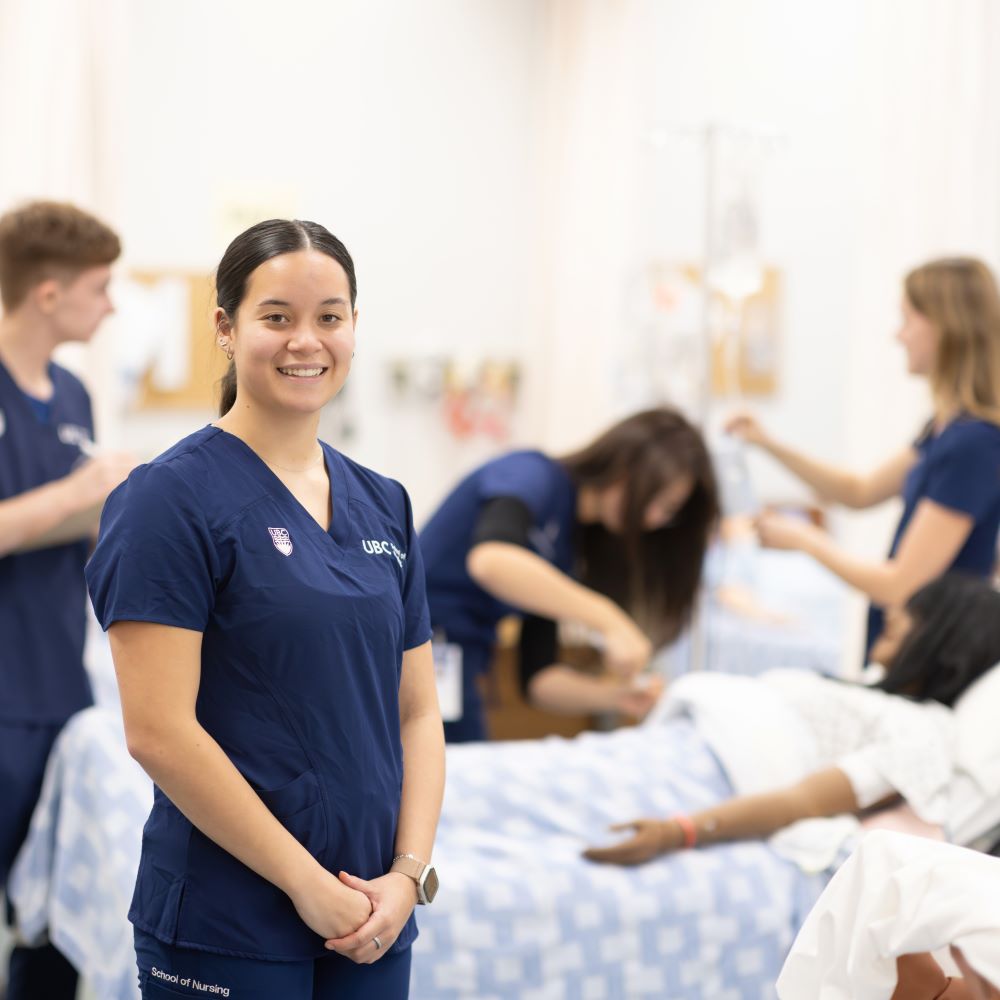 Nursing student standing in simulation lab with other students behind her.