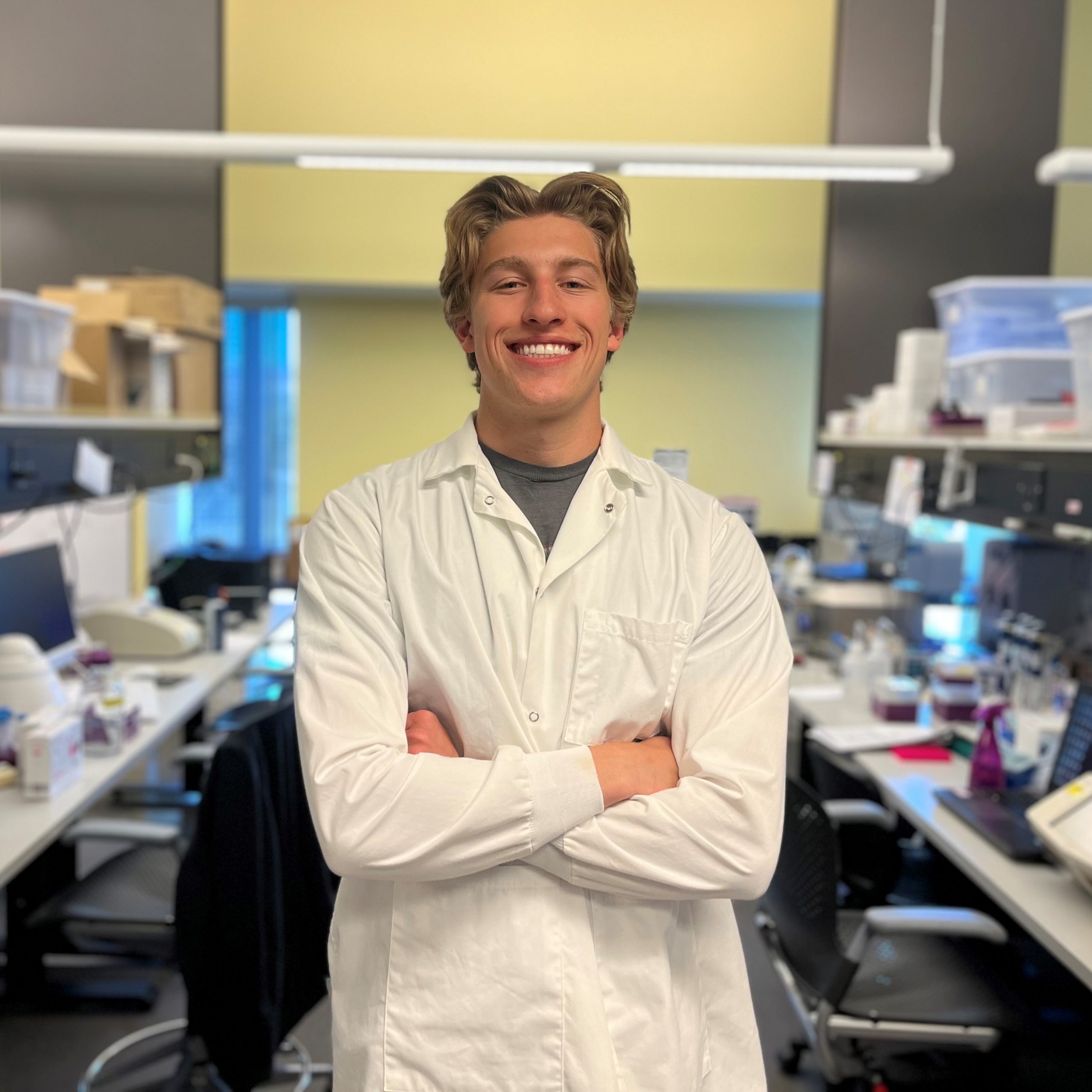 Graduate student in lab coat with arms crossed in lab.