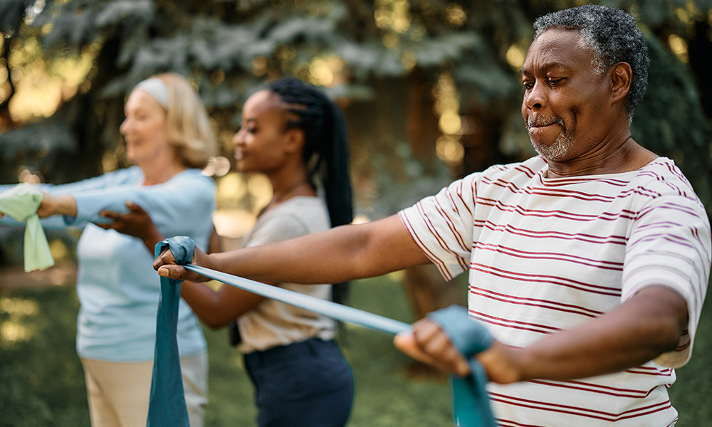 Black senior man using resistance band during exercise class in backyard of a nursing home.