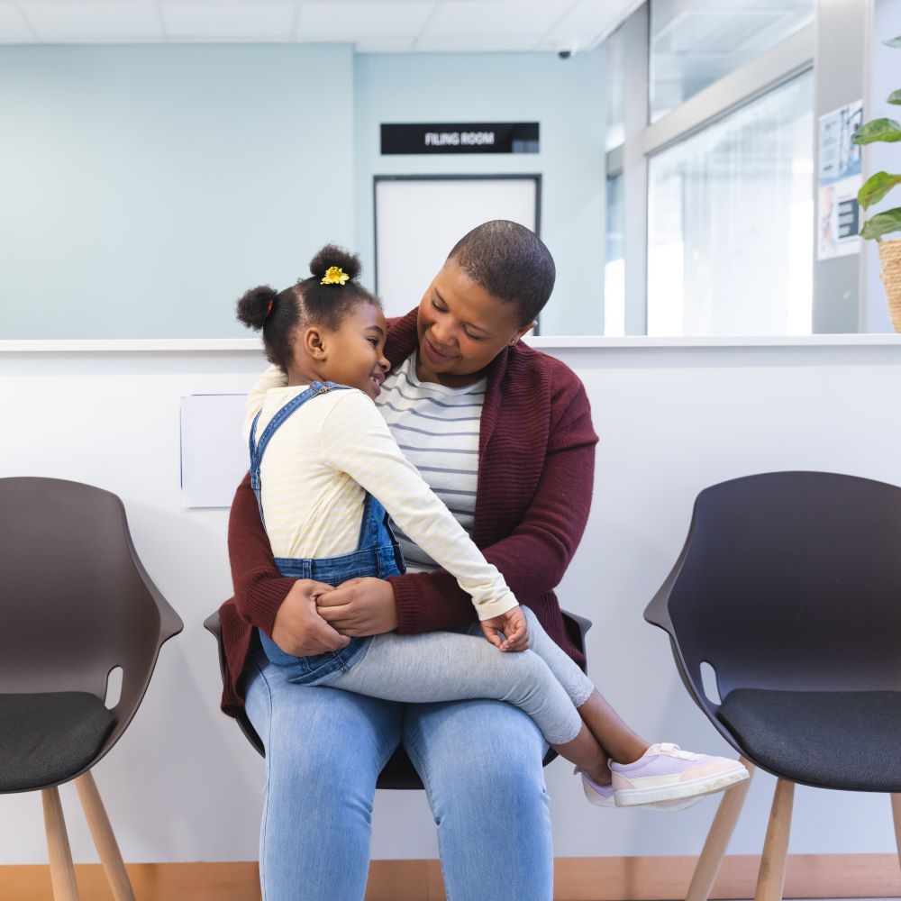 A woman holding her daughter on her lap in a health centre waiting room.